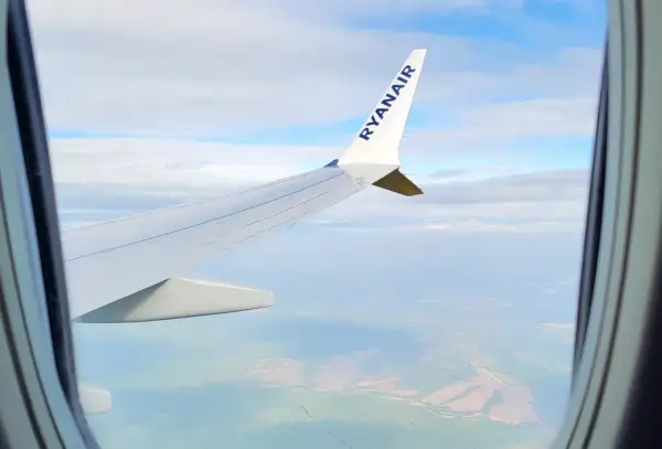 Widok z okna samolotu Ryanair, idealny do nauki, jak szukać tanich wakacji. Podróż nad zielonymi polami i chmurami.
