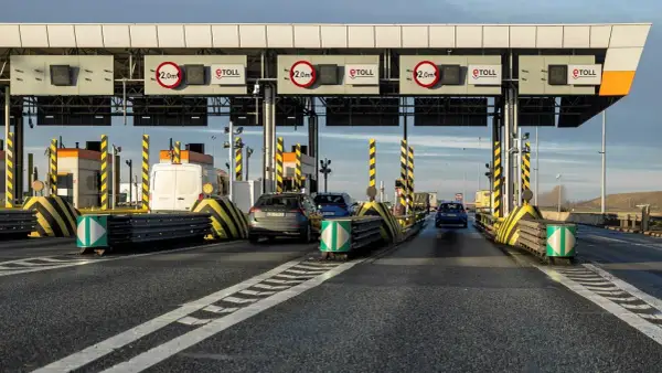 Samochody zbliżają się do bramek poboru opłat za autostrady. Widać znaki eTOLL i ograniczenia wysokości 2,0m.