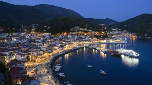 Widok na oświetlone miasto Parga nad morzem o zmierzchu, z górami w tle.