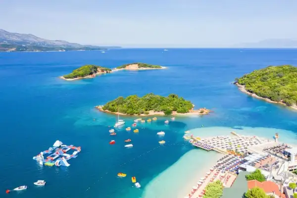 Malownicze **albania morze** z zielonymi wysepkami, plażą z leżakami i wodnym placem zabaw.