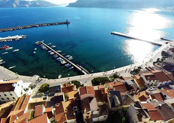 Widok na port i miasteczko Baška w Chorwacji. Woda jest turkusowa, a na nabrzeżu cumują łodzie.