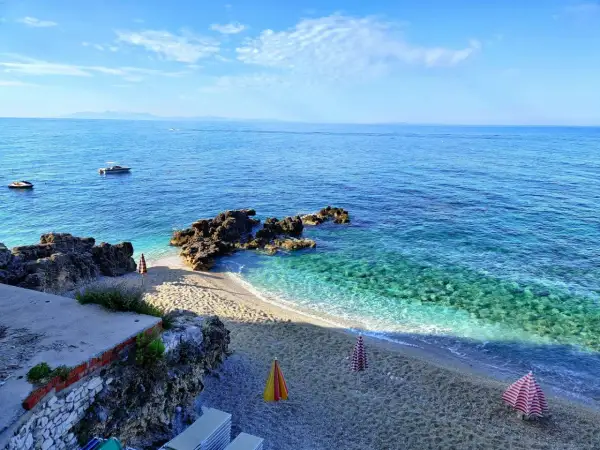 Albania, luty. Słoneczna pogoda nad turkusowym morzem, pusta plaża z leżakami i parasolami, łodzie na wodzie.
