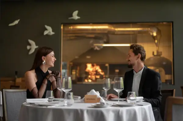 Elegancka para cieszy się romantyczną kolacją w restauracji a la carte all inclusive. Za nimi widać kuchnię z ogniem w piecu.
