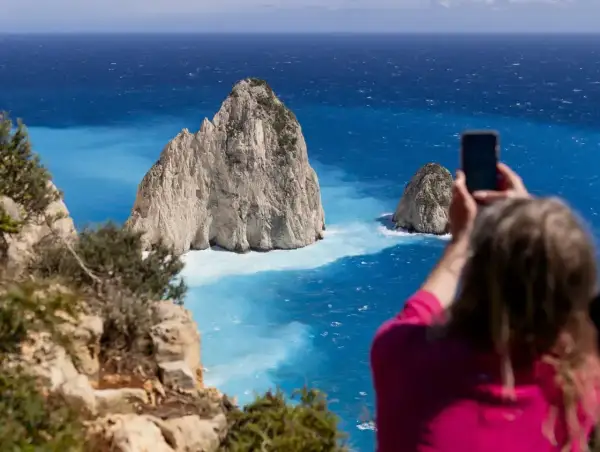 Widok na turkusowe morze Zakynthos, gdzie turystka robi zdjęcie skalistym wysepkom.