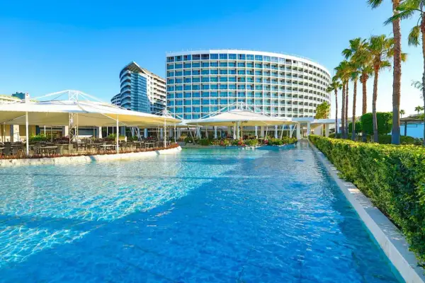 Luksusowy hotel z basenem i palmami. W oddali widać budynek w kształcie fali, a bliżej restaurację pod białymi markizami. Idealne miejsce na wypoczynek w Crystal Centro.
