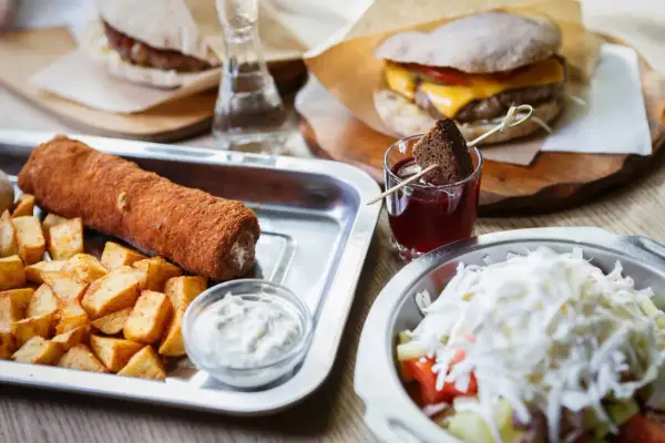 Sycące dania kuchni serbskiej: panierowany rolka mięsa z frytkami, burger i sałatka.
