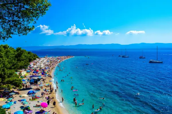 Wyspa Brać oferuje niezapomniane atrakcje: plaża Zlatni Rat tętni życiem, ludzie kąpią się w turkusowej wodzie, a żaglówki kołyszą się na morzu.