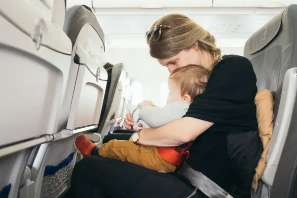 Mama tuli tulot z niemowlakiem w samolocie. Dziecko trzyma zabawkę z logo linii lotniczych.