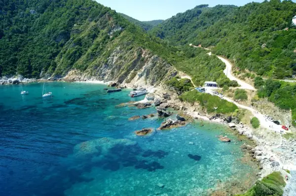 Malownicza zatoka na wyspie Skopelos z krystalicznie czystą wodą, łodziami i krętą drogą wiodącą przez zielone wzgórza.