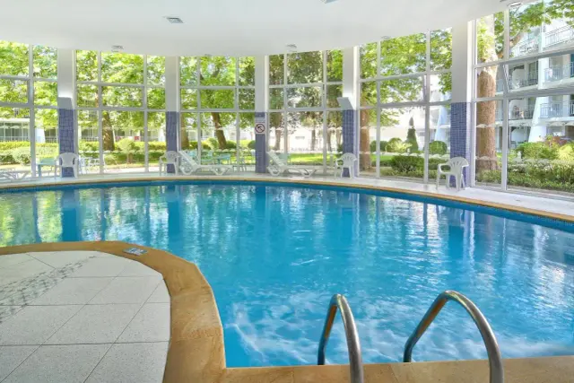 Wnętrze Ralitsa Aquaclub z basenem i dużymi oknami wychodzącymi na zielony ogród.